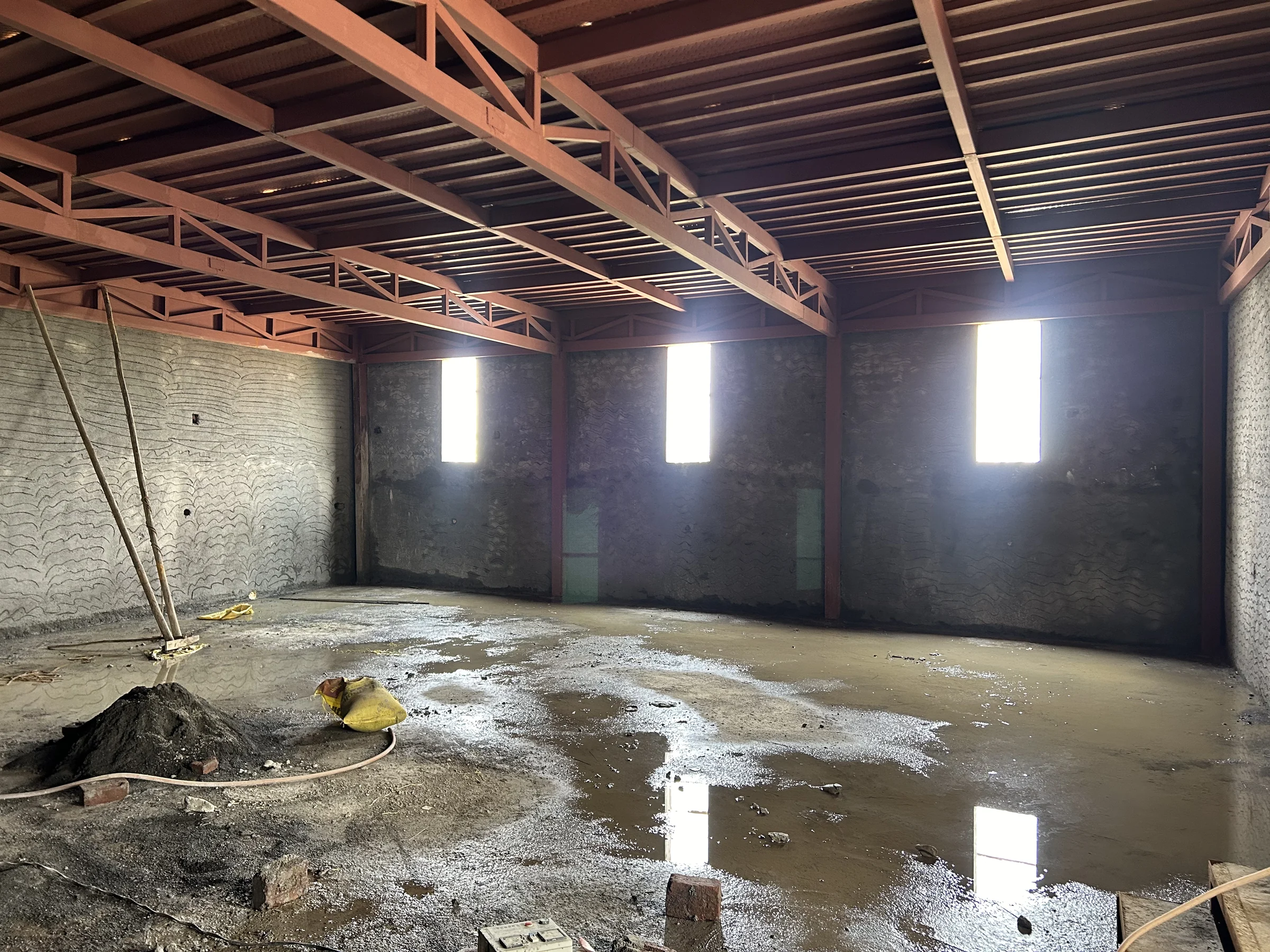 Site photograph: the unfinished dining hall under red-oxide steel trusses