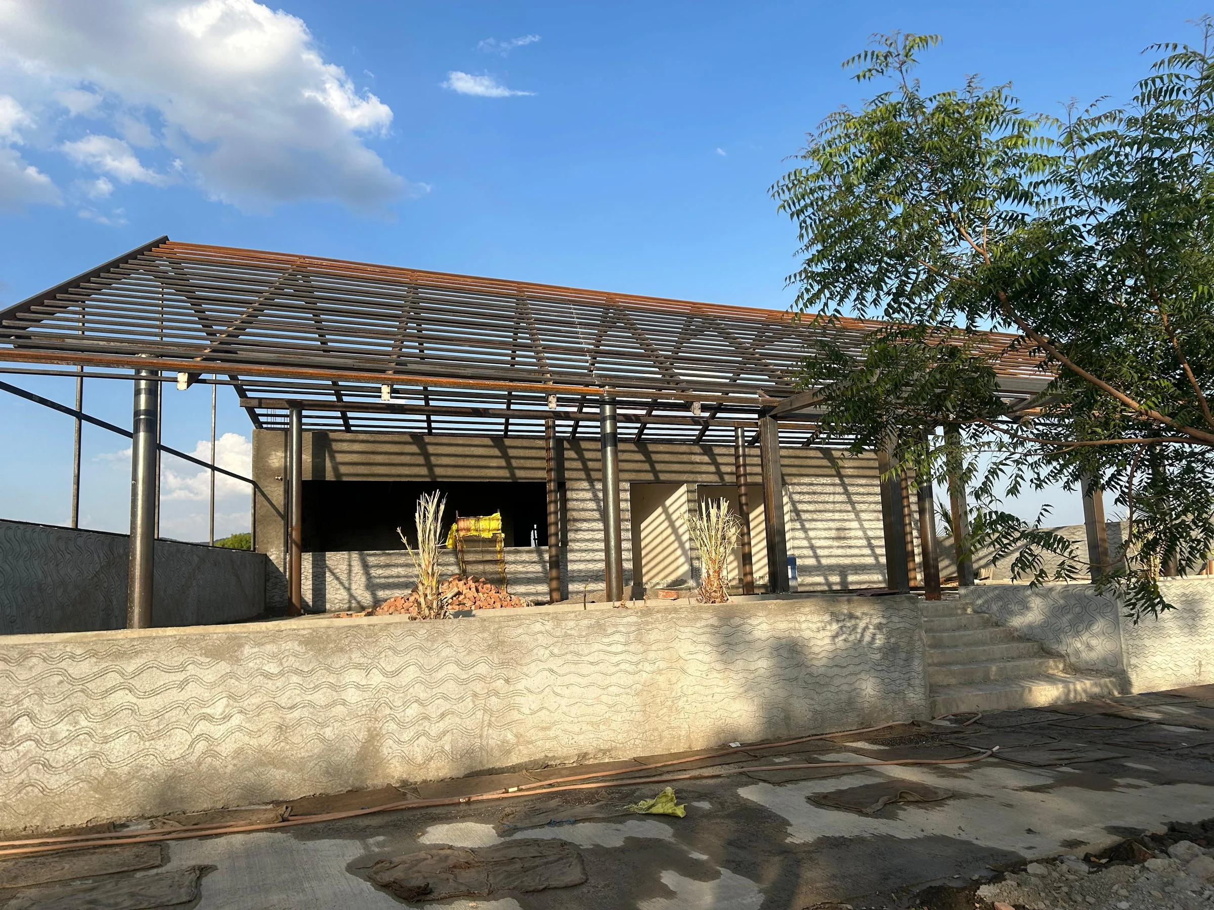 Site photograph: a concrete wall cast with a wave pattern below the open steel roof frame